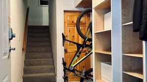 A hallway with a staircase, a bicycle leaning against a door, and a storage unit with shelves.