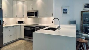 A modern kitchen with white cabinetry, a built-in microwave, a dishwasher, and a large island with a sink.