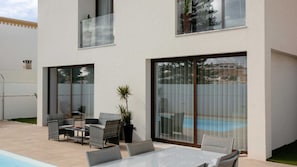 A modern outdoor patio with a pool, seating area, and large sliding glass doors. - Comfortable Villa Algarve for up to 10 guests (Alcantarilha)