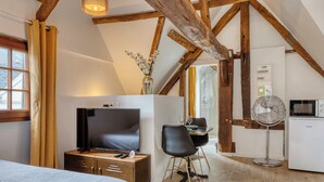 A bedroom with a bed, a TV, a desk with a chair, a fan, and a kitchenette. - Eveil 4 : le refuge lumière sous les toits de Rouen (Rouen)