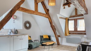 A cozy loft bedroom with exposed wooden beams, a modern kitchenette, and a view of the city through a large window. - Eveil 4 : le refuge lumière sous les toits de Rouen (Rouen)