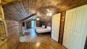 Un dormitorio abuhardinado con paneles de madera, techo inclinado, cama, armario y puerta.