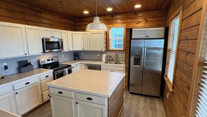 Una cocina moderna con paredes de madera, armarios blancos y electrodomésticos de acero inoxidable, con una isla central.