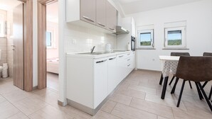 A modern kitchen with white cabinetry, a central island, and a dining area with a table and chairs. - Cozy apartment in Krusevo with WiFi (Krusevo)