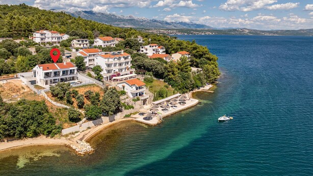 An aerial view of a coastal residential area with multiple buildings, a clear blue sea, and a mountainous backdrop. - Awesome home in Posedarje (Posedarje)
