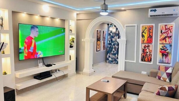 Un salon moderne doté d’un grand téléviseur à écran plat, d’un canapé, d’une table basse et d’une arche décorative.