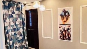 Un couloir moderne avec des rideaux à motifs géométriques, une porte noire et des œuvres d’art accrochées au mur.