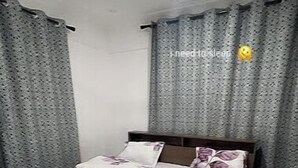 Une chambre à coucher avec un lit, des rideaux, un ventilateur de plafond et une table de chevet.