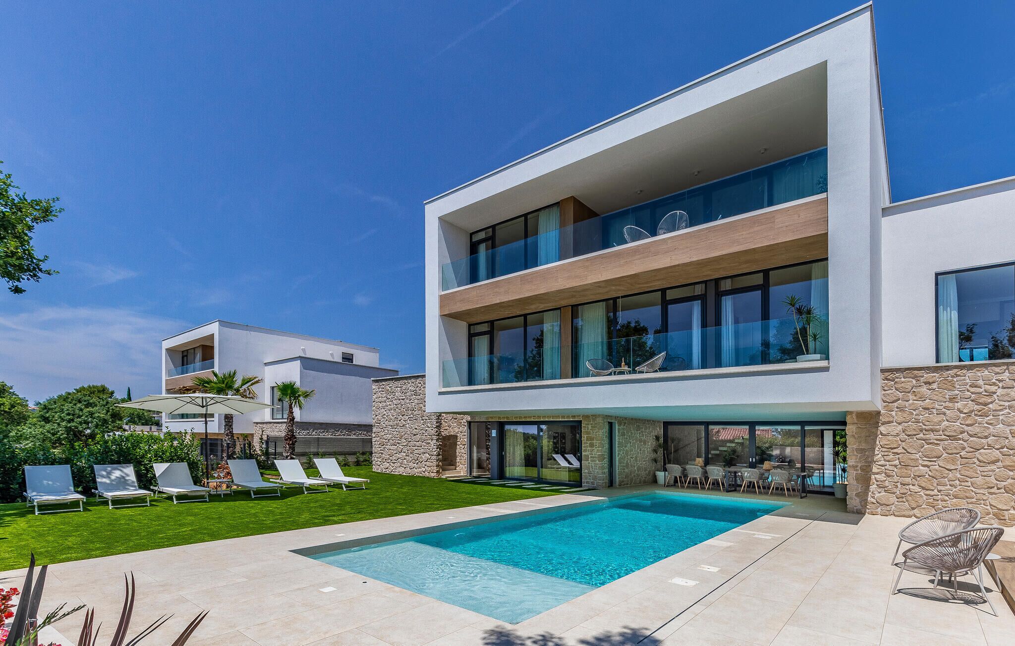 A modern two-story house with a swimming pool, outdoor seating, and a well-maintained lawn.