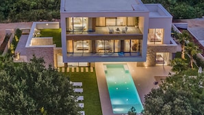 A modern two-story house with a large swimming pool, multiple balconies, and a well-maintained garden.