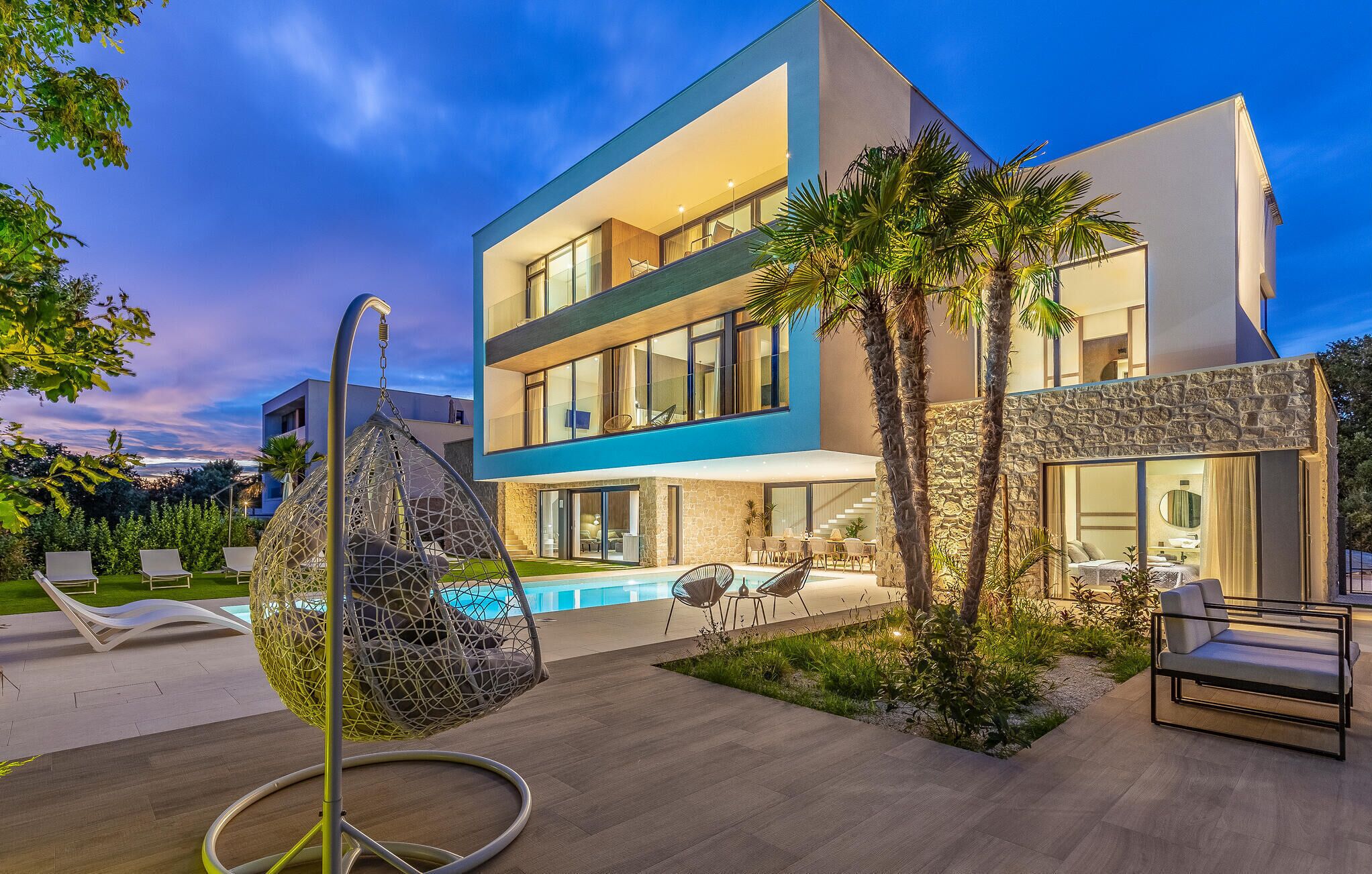 A modern two-story house with a swimming pool, outdoor seating, and a hanging chair.