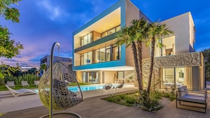 A modern two-story house with a swimming pool, outdoor seating, and a hanging chair.