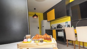 A compact kitchen with a dining area, featuring a wooden table with food and drinks, a microwave, and a refrigerator. - Maison Perdizes – Allianz Parque Supreme (Sao Paulo)