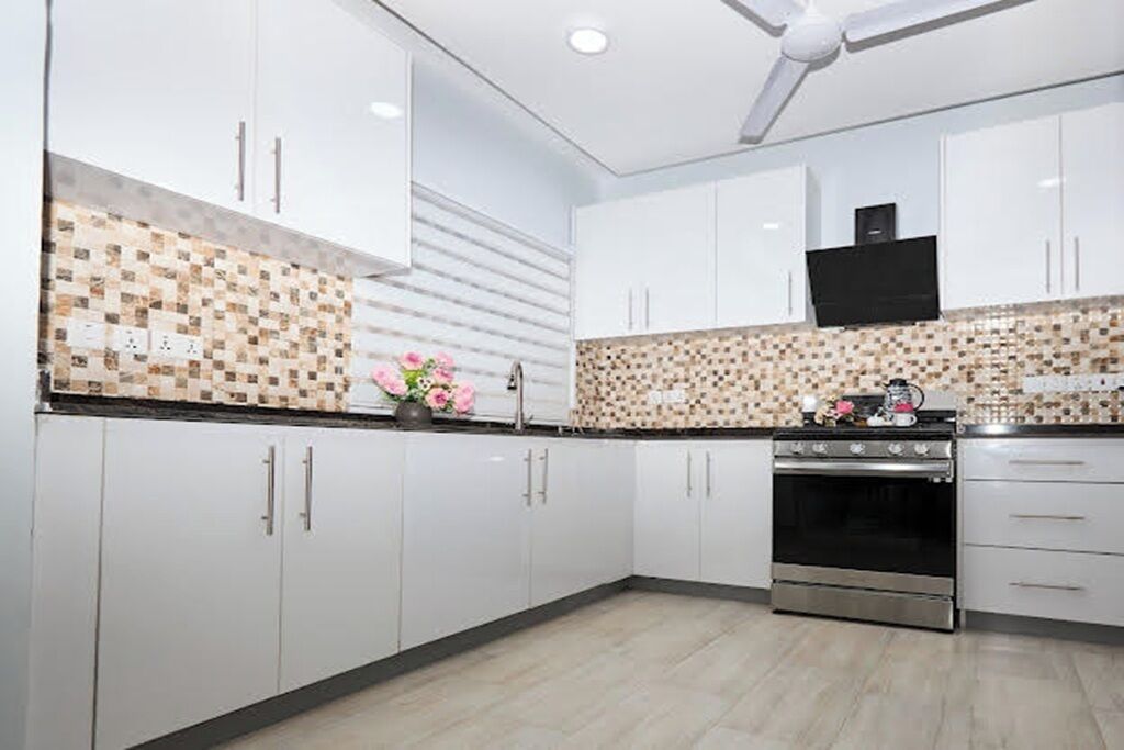 A modern kitchen with white cabinets, a tiled backsplash, a stainless steel oven, and a ceiling fan.