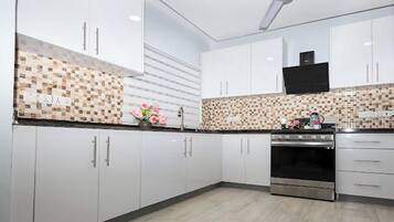 A modern kitchen with white cabinets, a tiled backsplash, a stainless steel oven, and a ceiling fan.