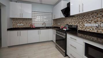 A modern kitchen with white cabinets, a black countertop, a tiled backsplash, a stove, and a ceiling fan.