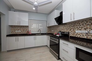 Une cuisine moderne avec des meubles blancs, un plan de travail noir, un pare-feu en carrelage, une cuisinière et un ventilateur de plafond.