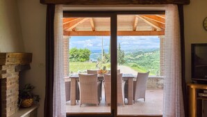 Une pièce dotée d’une porte-fenêtre coulissante donnant sur une terrasse extérieure avec une table et des chaises, une cheminée en briques et un téléviseur posé sur un meuble.