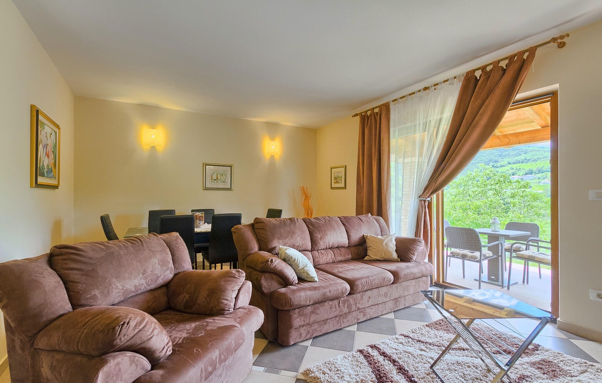 Een woonkamer met twee banken, een eettafel met stoelen en een uitzicht op een groen landschap door een glazen deur.