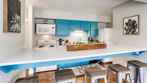 A modern kitchen with blue cabinets, white countertops, and a central island with stools.