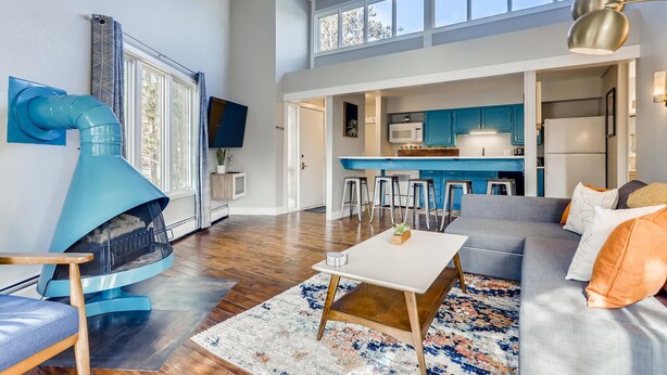 A spacious living room with a fireplace, a sofa, a coffee table, and a kitchen area with blue cabinets.
