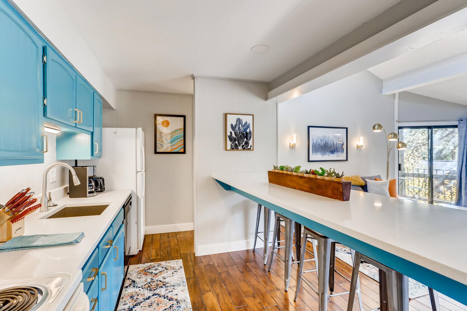 A modern kitchen with blue cabinets, a white countertop, and a wooden bar stool area.