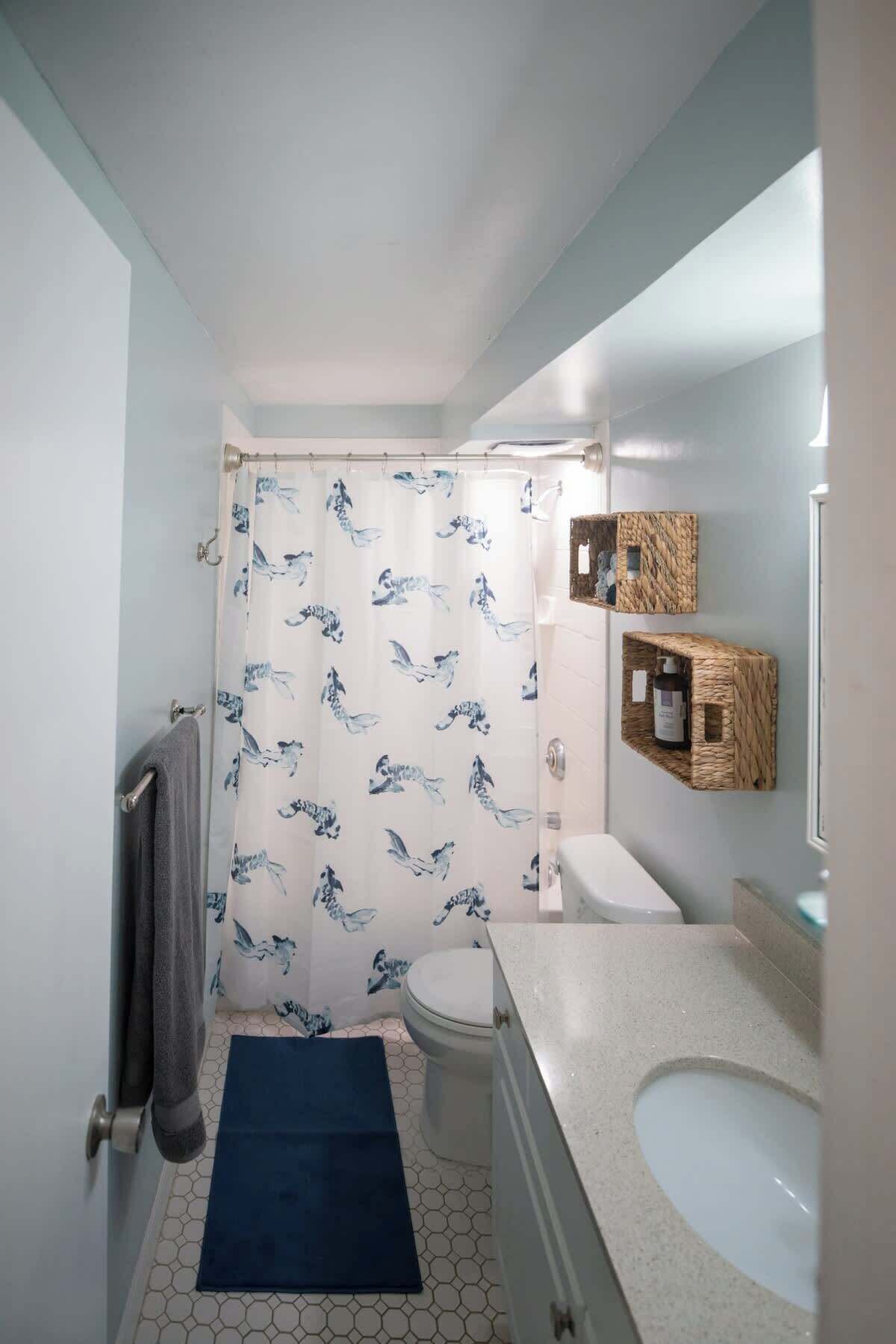 Une salle de bain avec un rideau de douche, des toilettes, un lavabo et un tapis bleu.