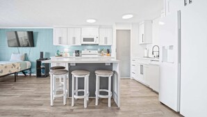 Une cuisine moderne avec des meubles blancs, un îlot central doté de tabourets, un téléviseur à écran plat et un plancher en bois.