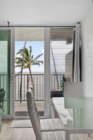 A room with a sliding glass door leading to a balcony with a view of the ocean and palm trees. - Beachfront Condo with Lanai and View (Hauula)