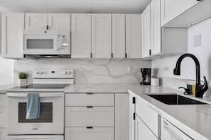 Una cocina moderna con armarios blancos, un microondas, un horno, una cafetera y un fregadero.