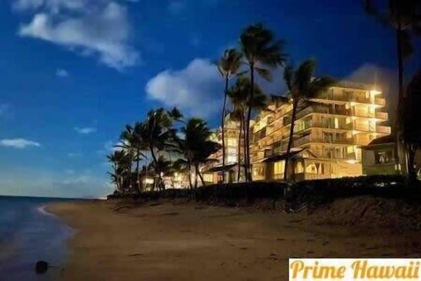 A beachfront hotel with multiple balconies, palm trees, and a sandy beach.