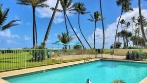 Une piscine à l’eau d’un bleu limpide, entourée d’une clôture, de palmiers et sous un ciel dégagé.