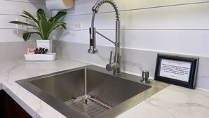 Et moderne køkken med en stålvask, en indbygget skraldespand og en potteplante.
