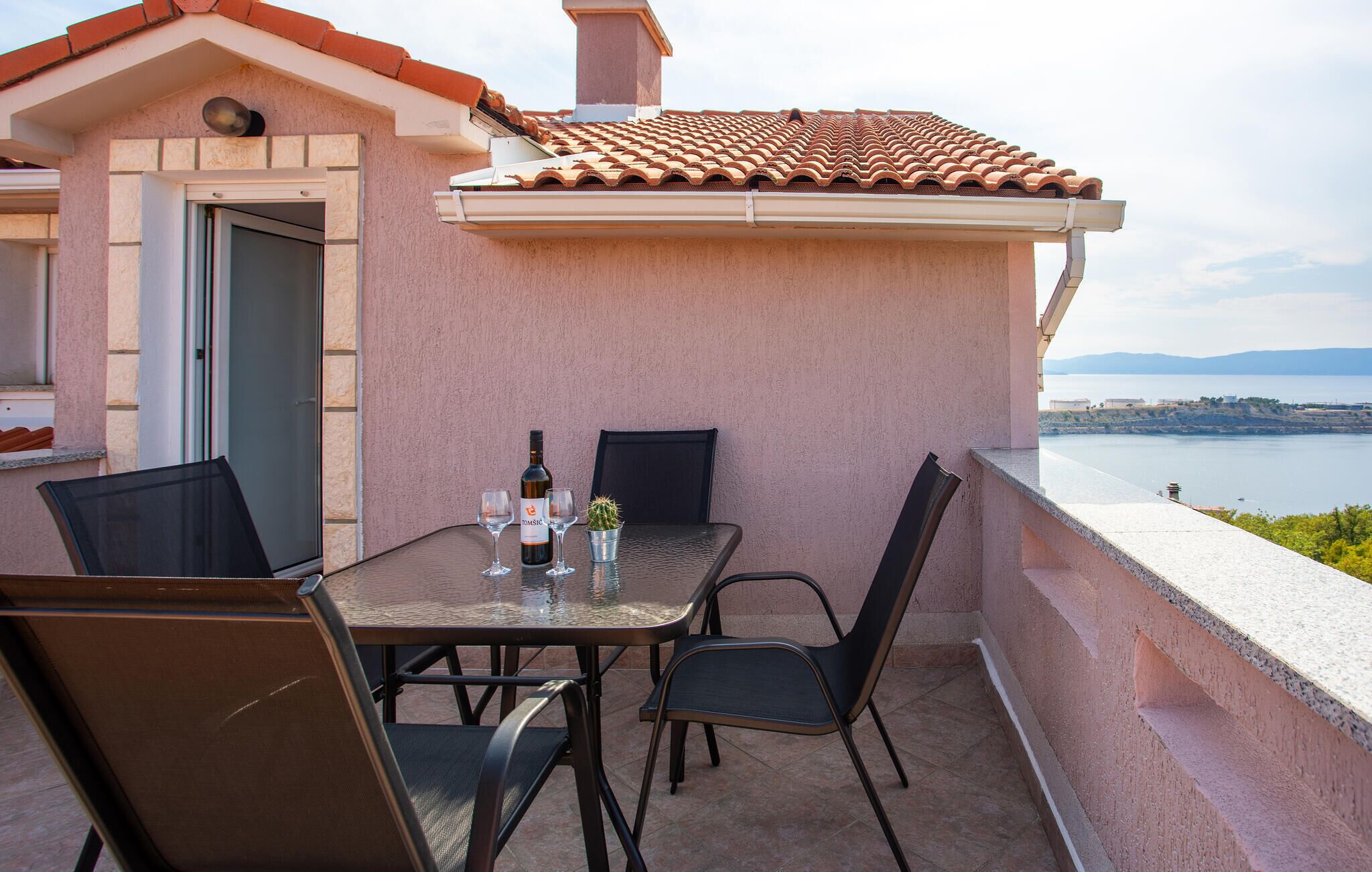 A balcony with a table and chairs, a bottle of wine, and a cactus.