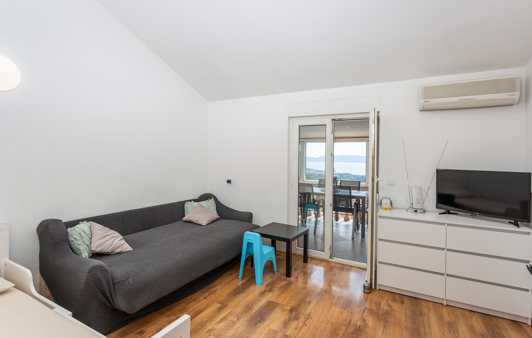 En moderne stue med sofa, et lille bord, et fjernsyn og en skydedør, der fører til et udendørs område.