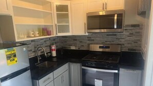 A compact kitchen with white cabinets, a stainless steel microwave, a gas stove, and a built-in oven.