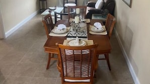 A dining area with a wooden table set for four, surrounded by wicker chairs.