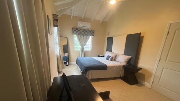 A bedroom with a bed, bedside tables, a desk, and an air conditioning unit.