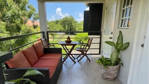 A balcony with a wicker sofa, a small table, and chairs. There is a potted plant on the floor.