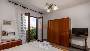 Un dormitorio con cama, un armario de madera, un televisor sobre un mueble de madera y vistas a través de un ventanal.