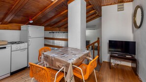 Una cocina acogedora con vigas de madera, una mesa de comedor con sillas anaranjadas, un refrigerador, una estufa y un televisor.