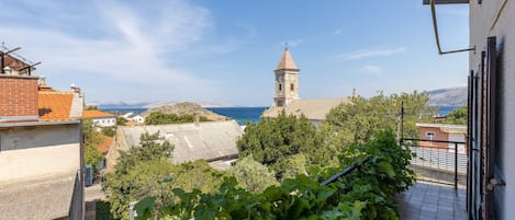 Vista d'una població costanera amb una imponent torre d'església, vegetació abundant i un cel blau clar.