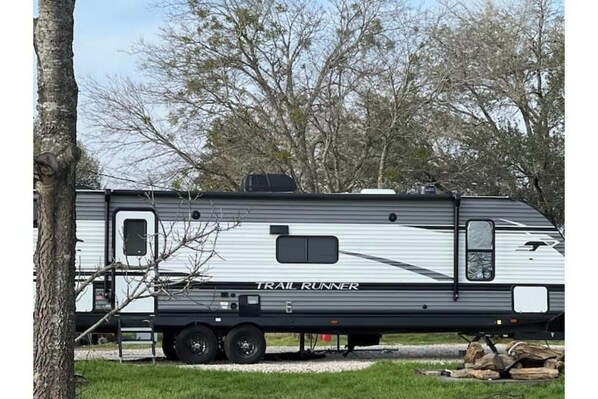 A Trail Runner RV parked in a grassy area with trees in the background. - The Backyard Camp (Lexington)
