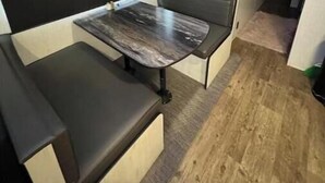 Une petite pièce avec une seule table et un banc, un luminaire au plafond et une fenêtre ornée de rideaux noirs.