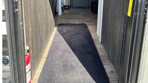 Un couloir étroit, doté d’une moquette sombre, mène à une pièce où se trouvent un lit et une petite table.