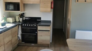 Una cocina compacta con armarios de madera, un microondas, una estufa y un lavamanos. Hay taburetes y una mesa pequeña.