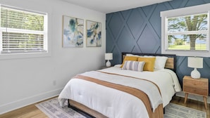 A bedroom with a bed, two bedside tables, a window with blinds, and abstract wall art. - Private home near Greensboro GSO Airport 20% off in checkout limited time (Kernersville)