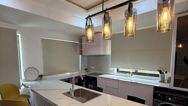A modern kitchen with a large island, pendant lights, and a built-in dishwasher.