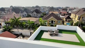 A rooftop with artificial grass, a seating area, and a view of surrounding residential buildings.