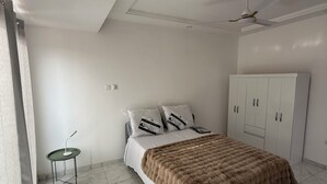 A bedroom with a bed, a wardrobe, a ceiling fan, and a small table.